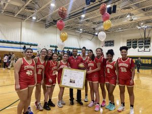 The girls varsity basketball team stands with Coach Eckert as they celebrate his 100th win on the court of the rivals.