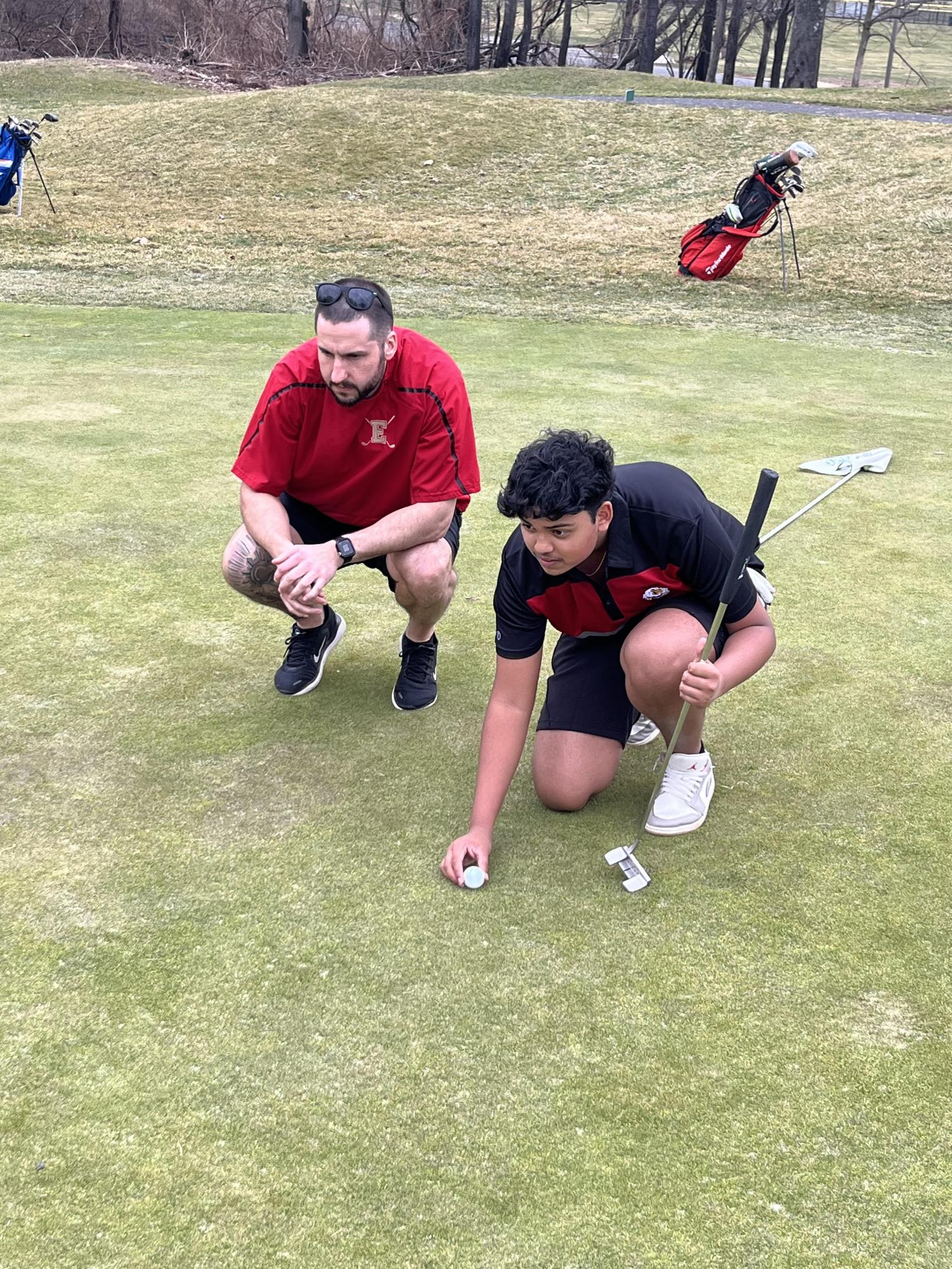 Boys Golf Coach Mr. Eric Breining assists Aarin Shrivastava '27 with lining up a putt. One of Breining's main goals as a coach is to teach his players to overcome adversity and adapt to the ever-changing environment of each course they play.