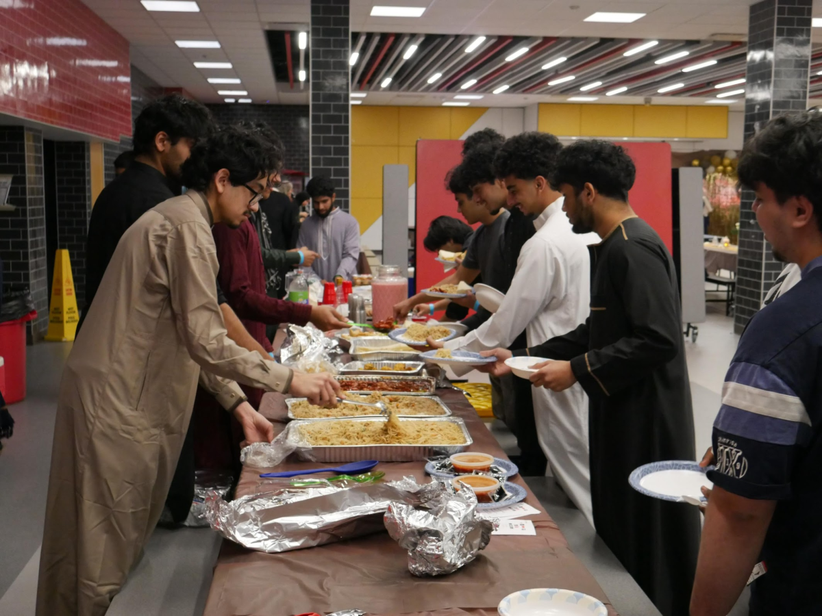 MSA members and students gather in the cafeteria to serve and share an iftar meal consisting of Chinese takeout and other foods, celebrating Ramadan tradition of gratitude and community.