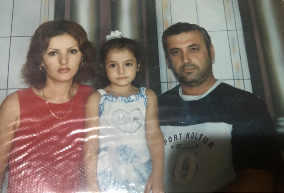 Kapaj, as a young girl, stands between her Albanian parents who came to the United States in 2007.